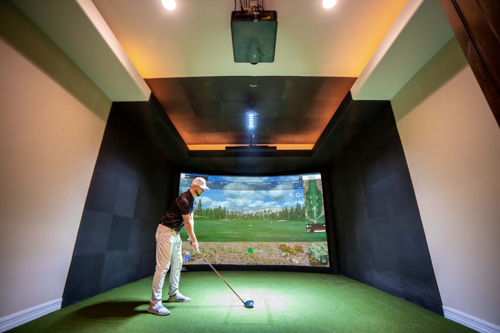 A man is enjoying a game of golf in a state-of-the-art indoor golf simulator.