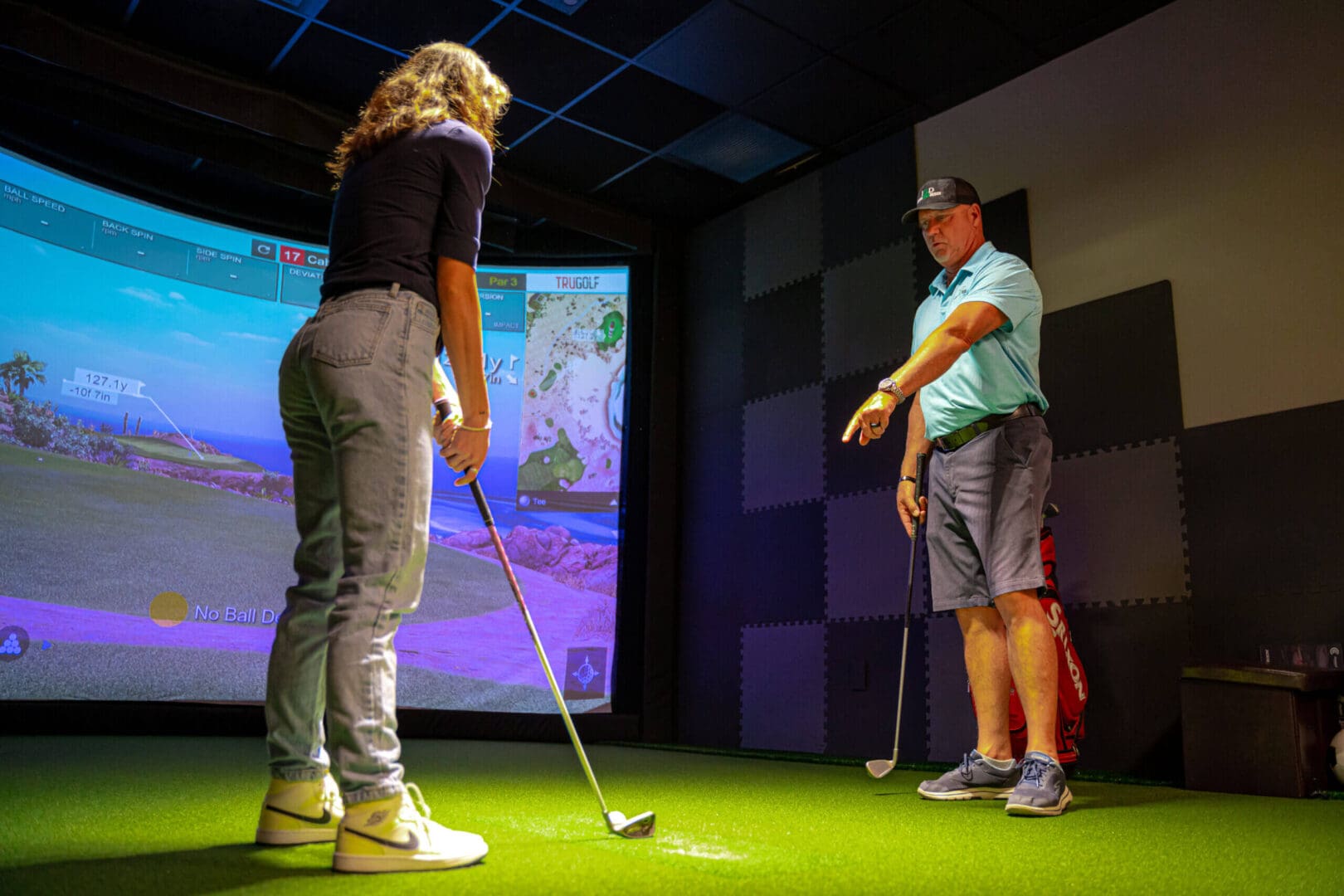 Two people playing Golf indoors in front of a screen