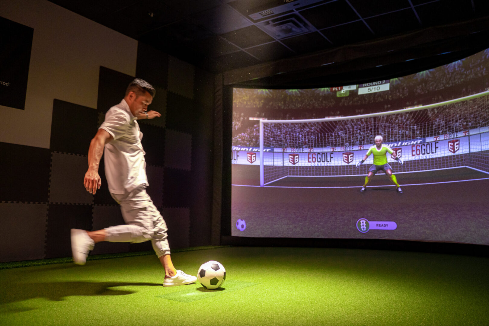 A man kicking a soccer ball in a video game room.