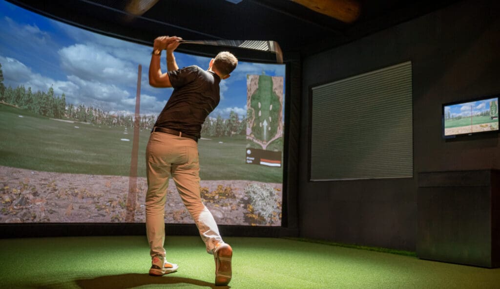 A man is playing golf in an indoor golf simulator.