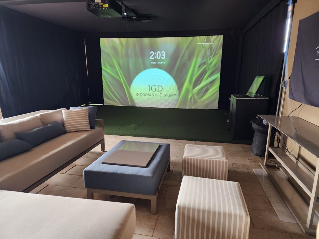 A room for a golf simulator with a large screen and couches.